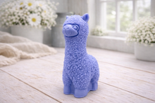Load image into Gallery viewer, handmade vegan soap in the shape of a realistic standing alpaca sculpture, featuring detailed curly wool texture and a smiling face, displayed on a rustic white wooden surface in a bright farmhouse decor setting.