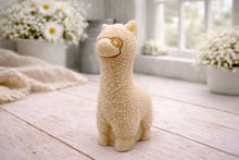 Load image into Gallery viewer, handmade vegan soap in the shape of a realistic standing alpaca sculpture, featuring detailed curly wool texture and a smiling face, displayed on a rustic white wooden surface in a bright farmhouse decor setting.