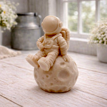 Load image into Gallery viewer, handmade vegan soap in the shape of a realistic astronaut sculpture sitting on the moon, featuring detailed spacesuit textures and craters on the lunar surface, displayed in a bright farmhouse decor setting.