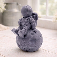 Load image into Gallery viewer, handmade vegan soap in the shape of a realistic astronaut sculpture sitting on the moon, featuring detailed spacesuit textures and craters on the lunar surface, displayed in a bright farmhouse decor setting.