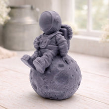 Load image into Gallery viewer, handmade vegan soap in the shape of a realistic astronaut sculpture sitting on the moon, featuring detailed spacesuit textures and craters on the lunar surface, displayed in a bright farmhouse decor setting.