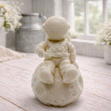 Load image into Gallery viewer, handmade vegan soap in the shape of a realistic astronaut sculpture sitting on the moon, featuring detailed spacesuit textures and craters on the lunar surface, displayed in a bright farmhouse decor setting.