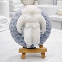 Load image into Gallery viewer, handmade vegan soap featuring a detailed astronaut sculpture floating against a detailed lunar surface background, displayed on a wooden easel.