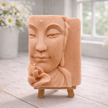 Load image into Gallery viewer, handmade vegan soap featuring a serene Buddha face relief with a lotus flower, displayed on a small wooden easel in a bright farmhouse decor setting with flowers and a rustic milk churn.