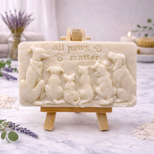Load image into Gallery viewer, handmade vegan soap featuring a detailed 3D relief of various dog breeds sitting in a row with the text "all paws matter," displayed on a wooden easel against a rustic farmhouse decor background.