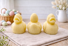 Load image into Gallery viewer, Three handmade vegan soaps in the shape of fluffy ducklings with open beaks, displayed on a neutral linen cloth in a bright farmhouse decor setting with Easter eggs in the background.