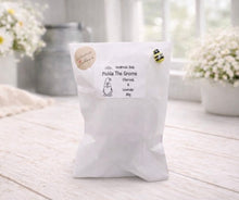 Load image into Gallery viewer, handmade vegan soap in the shape of a garden gnome sculpture with a long beard and a tall hat adorned with a large rose, displayed on a rustic white wooden surface in a bright farmhouse decor setting.