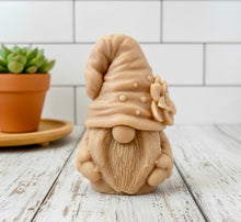 Load image into Gallery viewer, handmade vegan soap in the shape of a garden gnome sculpture with a long beard and a tall hat adorned with a large rose, displayed on a rustic white wooden surface in a bright farmhouse decor setting.