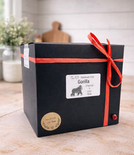 Load image into Gallery viewer, A large handmade vegan soap in the shape of a realistic sitting gorilla sculpture, featuring detailed muscular definition and skin texture, displayed on a rustic wooden surface in a farmhouse-style kitchen.