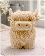 Load image into Gallery viewer, A detailed handmade vegan soap in a sculpted in the shape of a highland cow with characteristic long, wavy fur, horns, and a friendly face, displayed on a light wooden surface