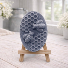 Load image into Gallery viewer, handmade vegan soap featuring an oval relief sculpture of two honey bees crawling on a honeycomb pattern, displayed on a small wooden easel in a bright farmhouse decor setting.