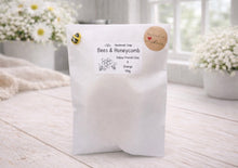 Load image into Gallery viewer, White soap packaging with a label on a light wooden surface, surrounded by flowers.