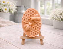 Load image into Gallery viewer, handmade vegan soap featuring an oval relief sculpture of two honey bees crawling on a honeycomb pattern, displayed on a small wooden easel in a bright farmhouse decor setting.