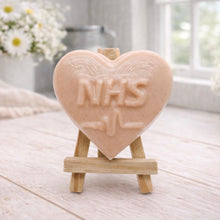 Load image into Gallery viewer, handmade vegan soap in a heart shape featuring an "NHS" relief and a heartbeat pulse line, displayed on a small wooden easel in a bright farmhouse decor setting.