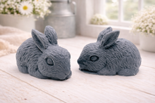 Load image into Gallery viewer, Set of two handmade vegan soaps in the shape of realistic crouching rabbits with detailed fur texture, displayed on a rustic white wooden surface in a bright farmhouse decor setting. Gift boxed.