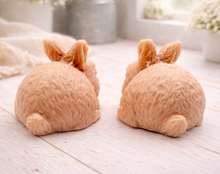 Load image into Gallery viewer, Set of two handmade vegan soaps in the shape of realistic crouching rabbits with detailed fur texture, displayed on a rustic white wooden surface in a bright farmhouse decor setting. Gift boxed.