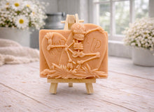 Load image into Gallery viewer, A handmade vegan soap depicting a skeleton resting between two R.I.P. gravestones, displayed on a small wooden easel.