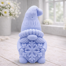 Load image into Gallery viewer, handmade vegan soap in the shape of a winter gnome sculpture holding a large snowflake, featuring a tall textured hat and a bushy mustache, displayed on a rustic white wooden surface with daisies and a milk churn in the background.
