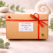 Load image into Gallery viewer, A set of three handmade vegan soaps in different sheep styles, including a dark grey smiling sheep and two lambs with detailed woolly textures, displayed on a rustic wooden surface with lavender and flowers.