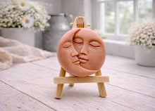 Load image into Gallery viewer, handmade vegan soap gift featuring a circular relief sculpture of a crescent moon and sun with peaceful intertwined faces, displayed on a small wooden easel in a bright farmhouse decor setting.