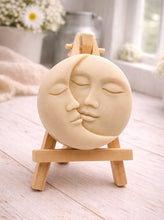 Load image into Gallery viewer, handmade vegan soap gift featuring a circular relief sculpture of a crescent moon and sun with peaceful intertwined faces, displayed on a small wooden easel in a bright farmhouse decor setting.