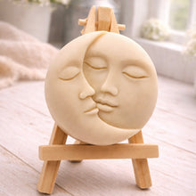 Load image into Gallery viewer, handmade vegan soap gift featuring a circular relief sculpture of a crescent moon and sun with peaceful intertwined faces, displayed on a small wooden easel in a bright farmhouse decor setting.