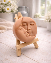 Load image into Gallery viewer, handmade vegan soap gift featuring a circular relief sculpture of a crescent moon and sun with peaceful intertwined faces, displayed on a small wooden easel in a bright farmhouse decor setting.