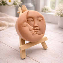 Load image into Gallery viewer, handmade vegan soap gift featuring a circular relief sculpture of a crescent moon and sun with peaceful intertwined faces, displayed on a small wooden easel in a bright farmhouse decor setting.