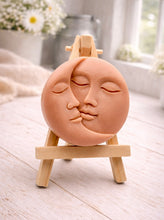 Load image into Gallery viewer, handmade vegan soap gift featuring a circular relief sculpture of a crescent moon and sun with peaceful intertwined faces, displayed on a small wooden easel in a bright farmhouse decor setting.