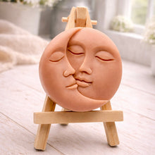 Load image into Gallery viewer, handmade vegan soap gift featuring a circular relief sculpture of a crescent moon and sun with peaceful intertwined faces, displayed on a small wooden easel in a bright farmhouse decor setting.