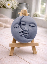 Load image into Gallery viewer, handmade vegan soap gift featuring a circular relief sculpture of a crescent moon and sun with peaceful intertwined faces, displayed on a small wooden easel in a bright farmhouse decor setting.