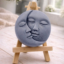 Load image into Gallery viewer, handmade vegan soap gift featuring a circular relief sculpture of a crescent moon and sun with peaceful intertwined faces, displayed on a small wooden easel in a bright farmhouse decor setting.