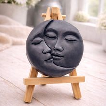 Load image into Gallery viewer, handmade vegan soap gift featuring a circular relief sculpture of a crescent moon and sun with peaceful intertwined faces, displayed on a small wooden easel in a bright farmhouse decor setting.