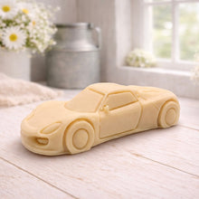 Load image into Gallery viewer, handmade vegan soap in the shape of a sleek supercar sculpture, featuring aerodynamic curves and detailed wheels, displayed on a rustic white wooden surface in a bright farmhouse decor setting.