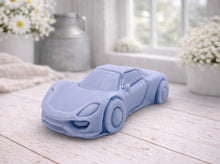 Load image into Gallery viewer, handmade vegan soap in the shape of a sleek supercar sculpture, featuring aerodynamic curves and detailed wheels, displayed on a rustic white wooden surface in a bright farmhouse decor setting.