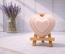 Load image into Gallery viewer, handmade vegan soap gift featuring a triple-tiered heart relief design, displayed on a wooden easel against a rustic farmhouse decor background with lavender.