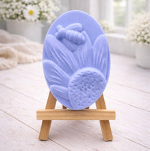 Load image into Gallery viewer, A handmade vegan soap in a natural colour, featuring an oval relief of a honeybee landing on a large sunflower with detailed petals and a textured centre, displayed on a small wooden easel.