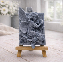 Load image into Gallery viewer, A rectangular handmade vegan soap, featuring a high-relief carving of a seated fairy with large, detailed wings holding a single blossom, displayed on a miniature wooden easel.