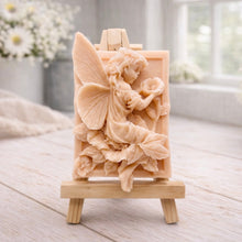 Load image into Gallery viewer, A rectangular handmade vegan soap, featuring a high-relief carving of a seated fairy with large, detailed wings holding a single blossom, displayed on a miniature wooden easel.