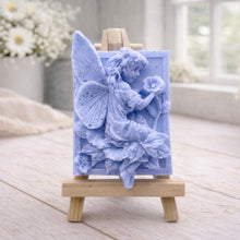 Load image into Gallery viewer, A rectangular handmade vegan soap, featuring a high-relief carving of a seated fairy with large, detailed wings holding a single blossom, displayed on a miniature wooden easel.