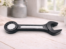 Load image into Gallery viewer, A handmade vegan soap sculpted in the shape of a realistic spanner or wrench tool, finished in a sleek charcoal black with silver-painted detailing on the handle and head, lying on a light wood surface.
