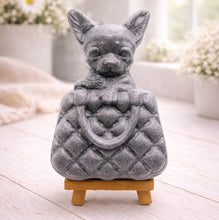 Load image into Gallery viewer, A highly detailed handmade vegan soap in a speckled grey marble finish, sculpted as a small chihuahua puppy with large ears peeking out from inside a quilted designer-style handbag, displayed on a miniature wooden easel.