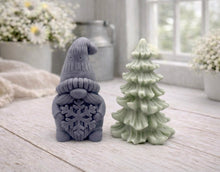 Load image into Gallery viewer, A pair of handmade vegan soaps featuring a Christmas gonk (gnome) with a textured hat holding a large snowflake, standing next to a pale mint-green 3D Christmas tree with layered, snow-dusted branches, displayed in a bright farmhouse setting.