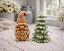 Load image into Gallery viewer, A pair of handmade vegan soaps featuring a Christmas gonk (gnome) with a textured hat holding a large snowflake, standing next to a pale mint-green 3D Christmas tree with layered, snow-dusted branches, displayed in a bright farmhouse setting.