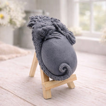 Load image into Gallery viewer, A 3D handmade vegan soap in a charcoal-grey tone, sculpted as a large prehistoric egg with a small dinosaur or dragon clinging to the top, featuring detailed scales and a curled tail, displayed on a miniature wooden easel.