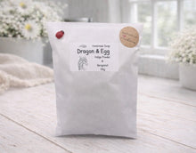 Load image into Gallery viewer, White bag labeled 'Dragon & Egg' on a wooden surface with flowers in the background
