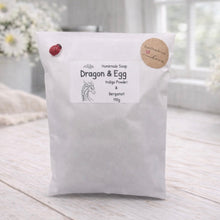 Load image into Gallery viewer, White bag labeled 'Dragon & Egg' on a wooden surface with flowers in the background