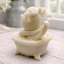 Load image into Gallery viewer, A handmade vegan soap is sculpted in the shape of a "dirty cow" character happily sitting in a bubble-filled roll-top bathtub with one hoof raised, displayed on a light wooden surface.