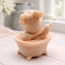 Load image into Gallery viewer, A handmade vegan soap is sculpted in the shape of a "dirty cow" character happily sitting in a bubble-filled roll-top bathtub with one hoof raised, displayed on a light wooden surface.