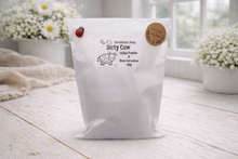 Load image into Gallery viewer, White bag labeled 'Dirty Cow' on a wooden surface with flowers in the background